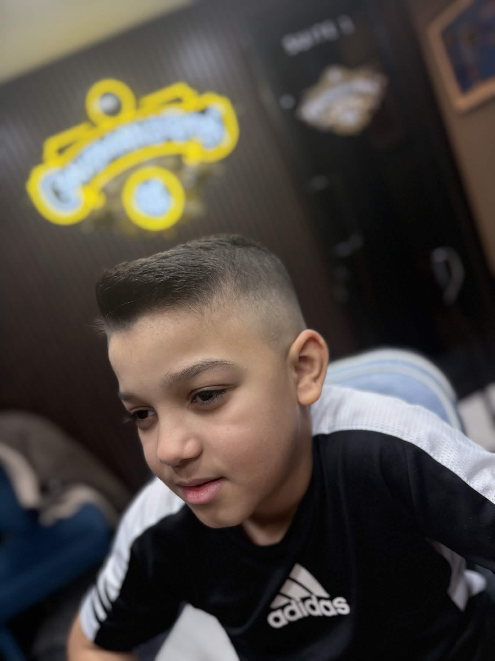 Kids taper fade with side part — Caveman's Den neon sign in background